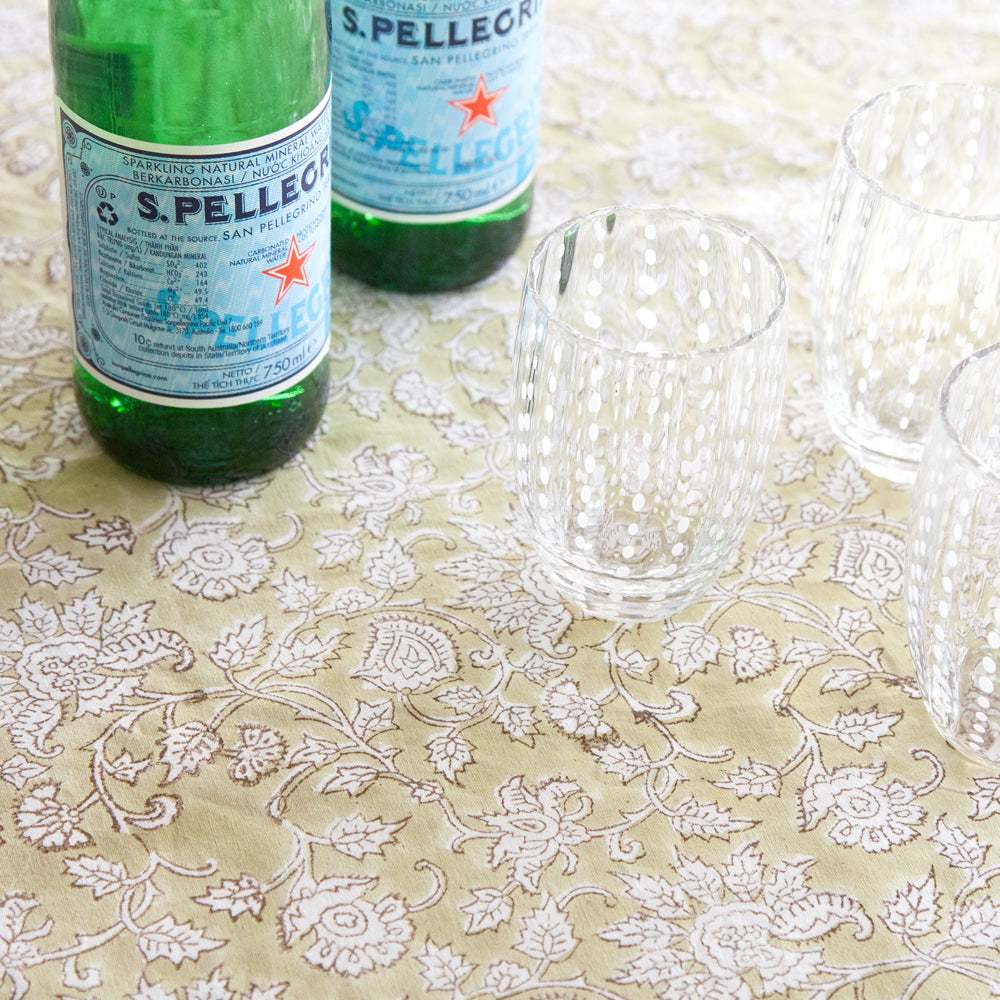 Green paisley block printed tablecloth with green bottles and clear glasses.