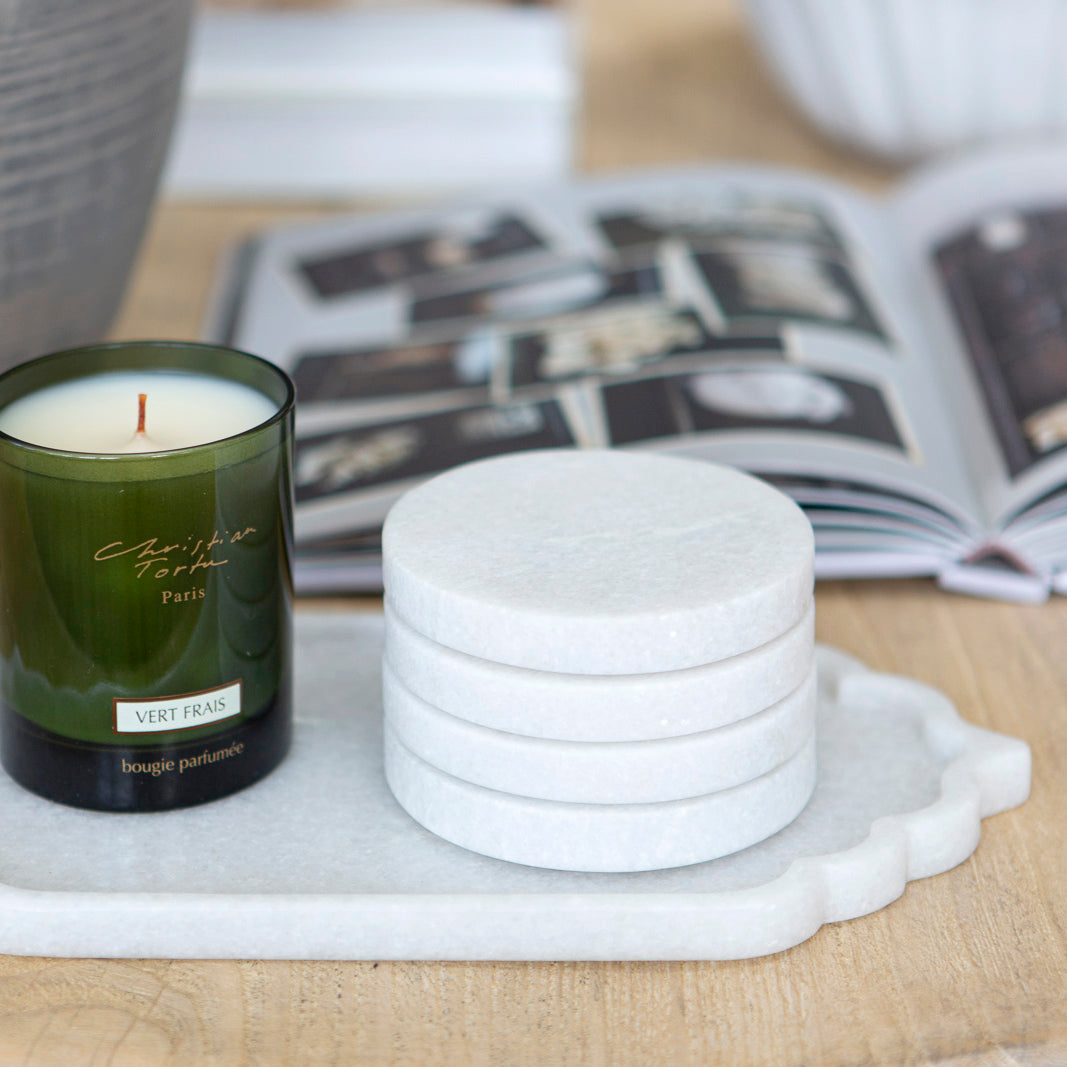 Stack of round marble coasters on a marble tray with a green glass candle.