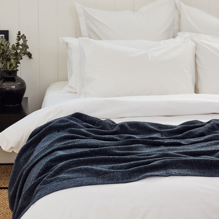 Blue Bemboka cotton throw draped across a bed with white bed linen.