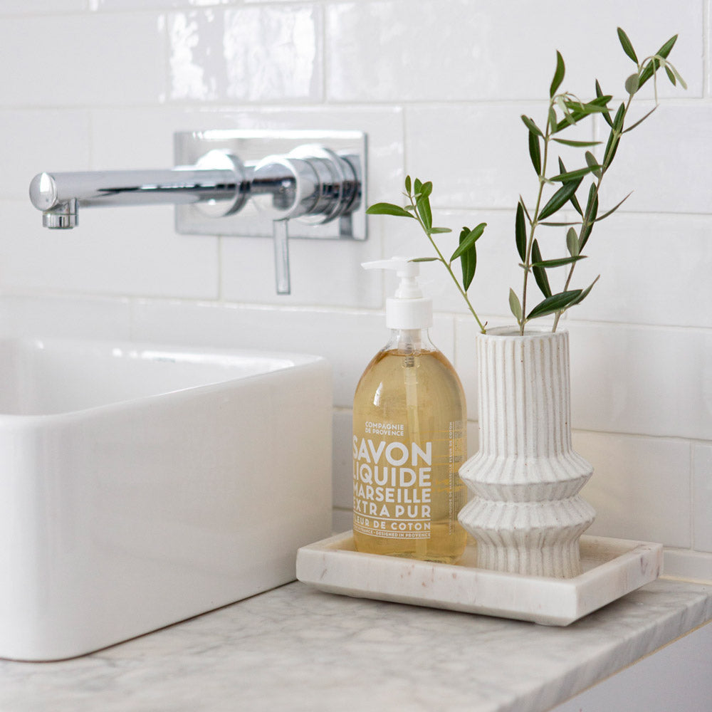 Compagne De Provence Cotton Flower hand soap in bathroom. Displayed on bathroom vanity on marble tray with ceramic vase. 