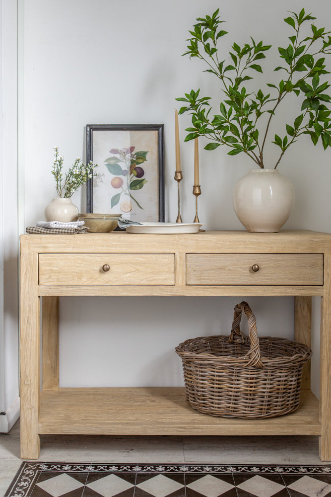 A console table styled with an artwork, a lamp, books, and vases. 