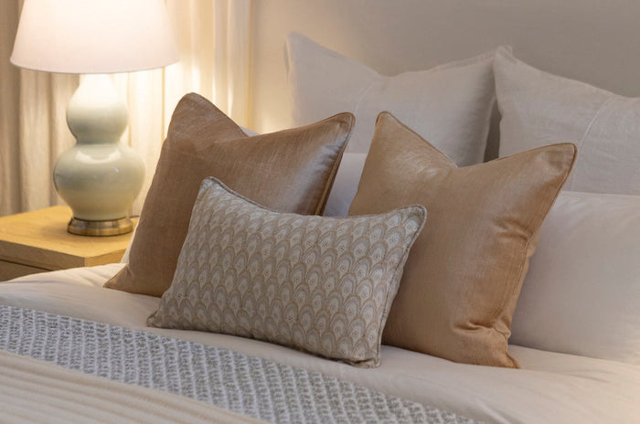 Decorative cushions styled on a bed with warm lamp light.