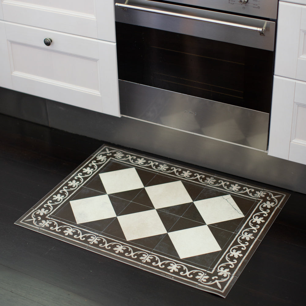 Beija Flor Gambit vinyl floor mat. Black and antique white check tile look mat in kitchen in front of oven.