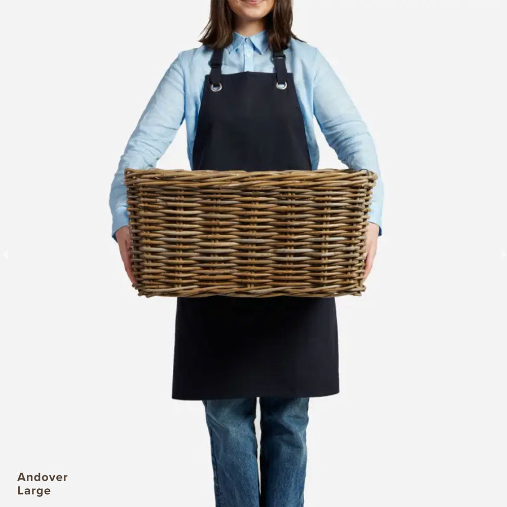 Lady in apron holding rectangular wicker storage basket. 