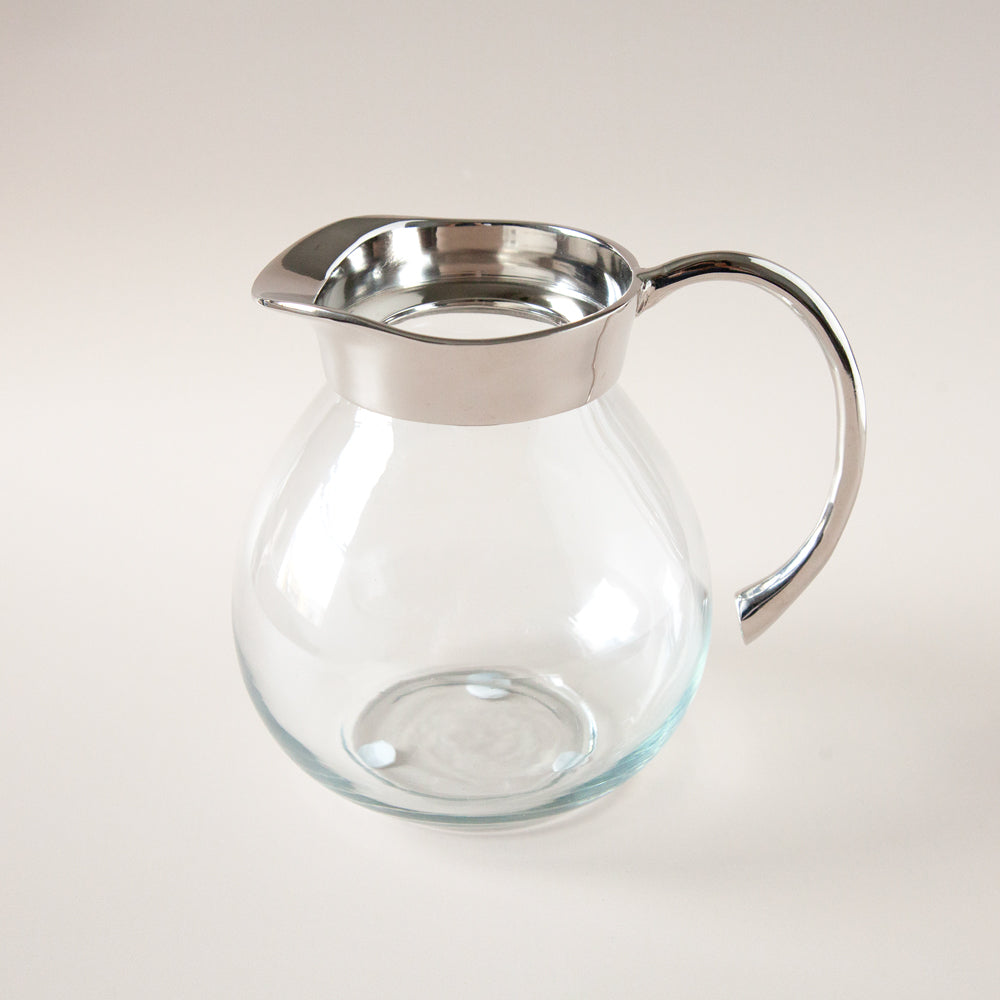 Clear glass jug with metal spout and handle.