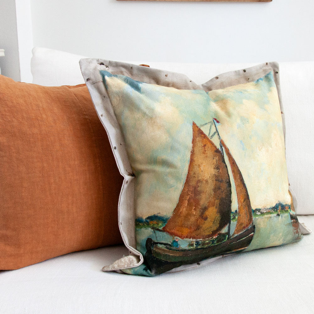 Cushion featuring painting of sail boats on a lake.