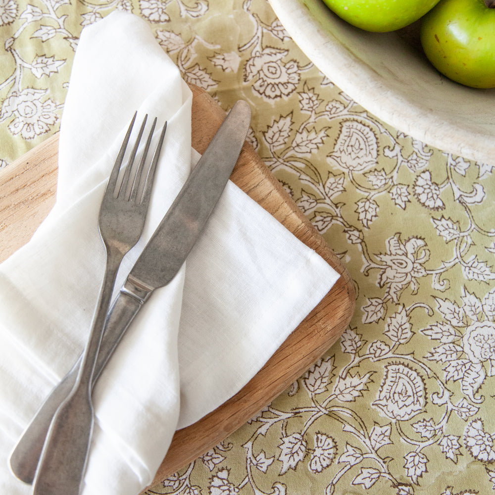 Green paisley block printed tablecloth with wooden board, napkin and cutlery.