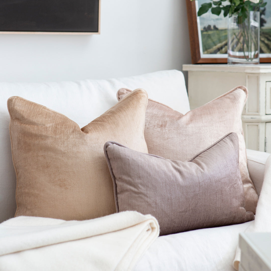 Three different coloured velvet cushions on white sofa.