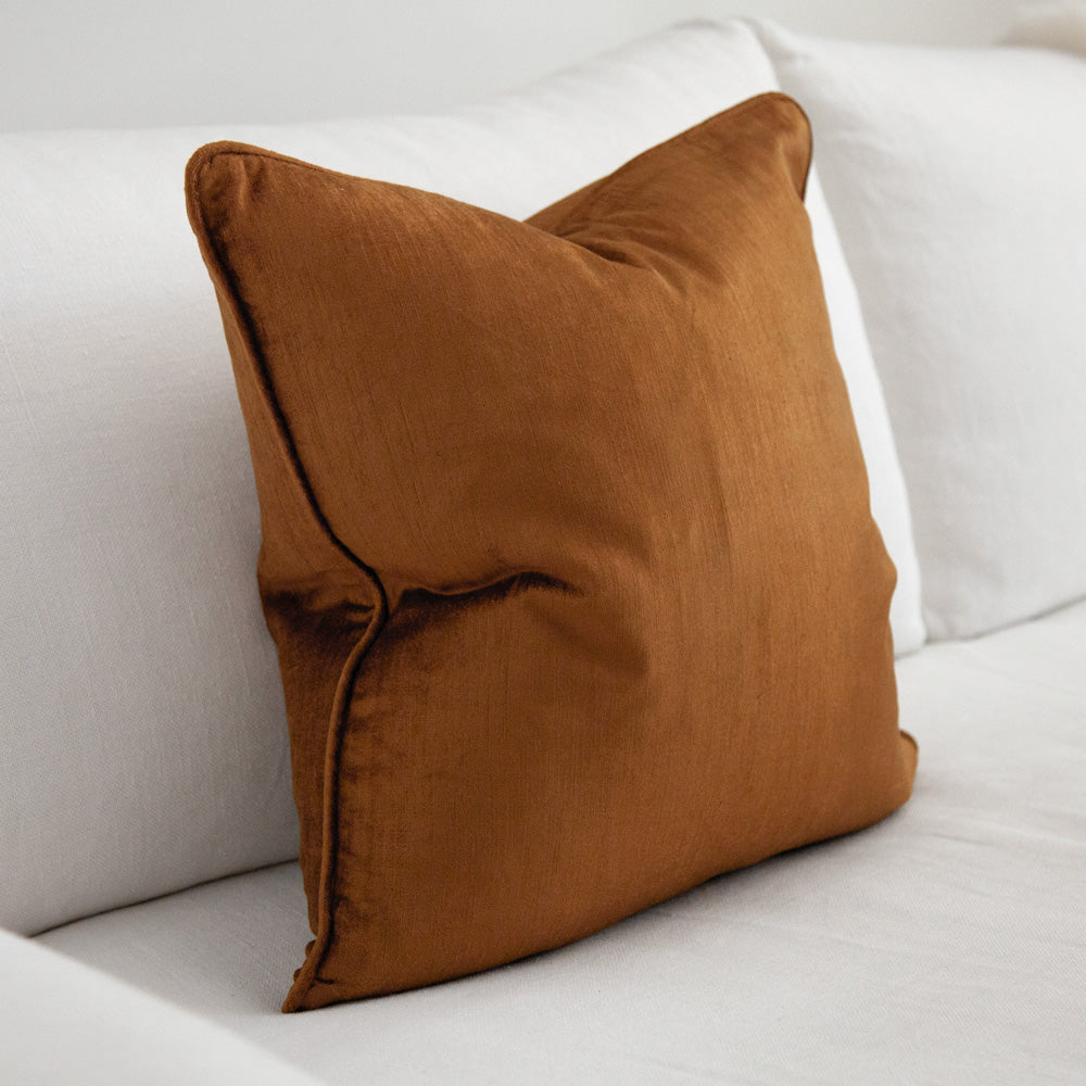 Ochre coloured square velvet cushion with piping.