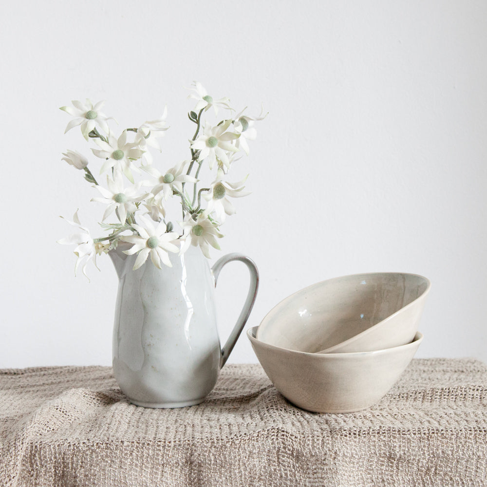 Glazed ceramic jug with flannel flowers sitting on table next two two ceramic bowls.