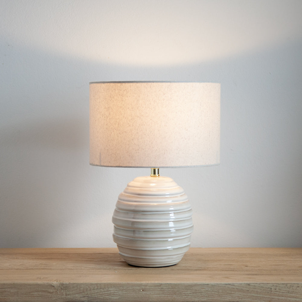 Small ceramic lamp with linen shade turned on.