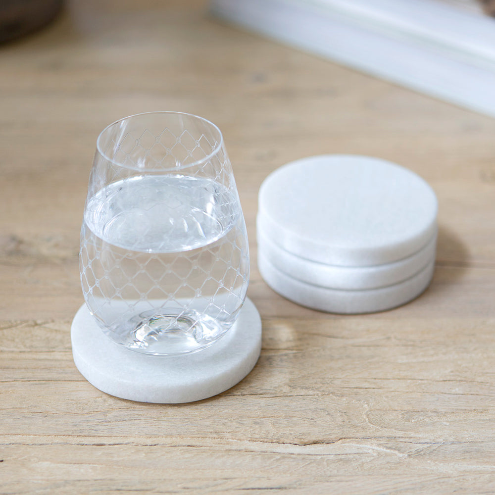 Round white marble coasters. Three in a stack and one in use with a glass of water.