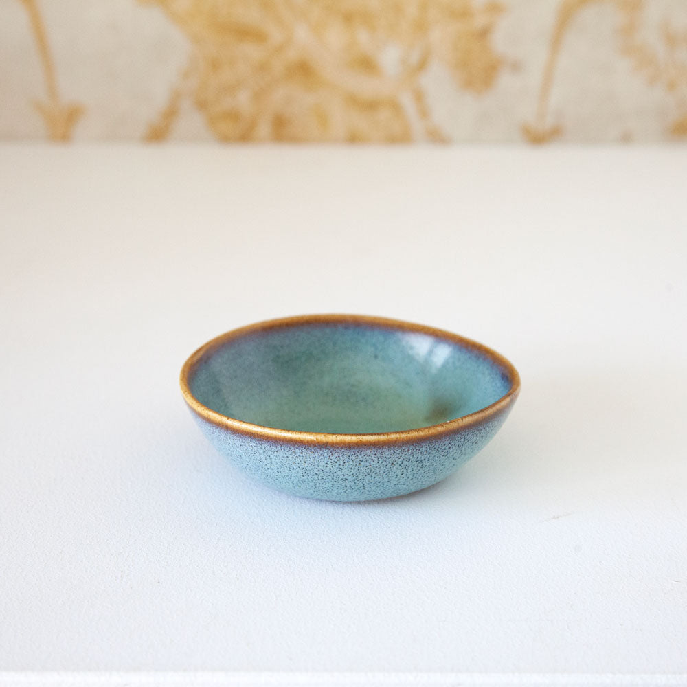 Small ceramic bowl with turquoise glaze and brown rim.