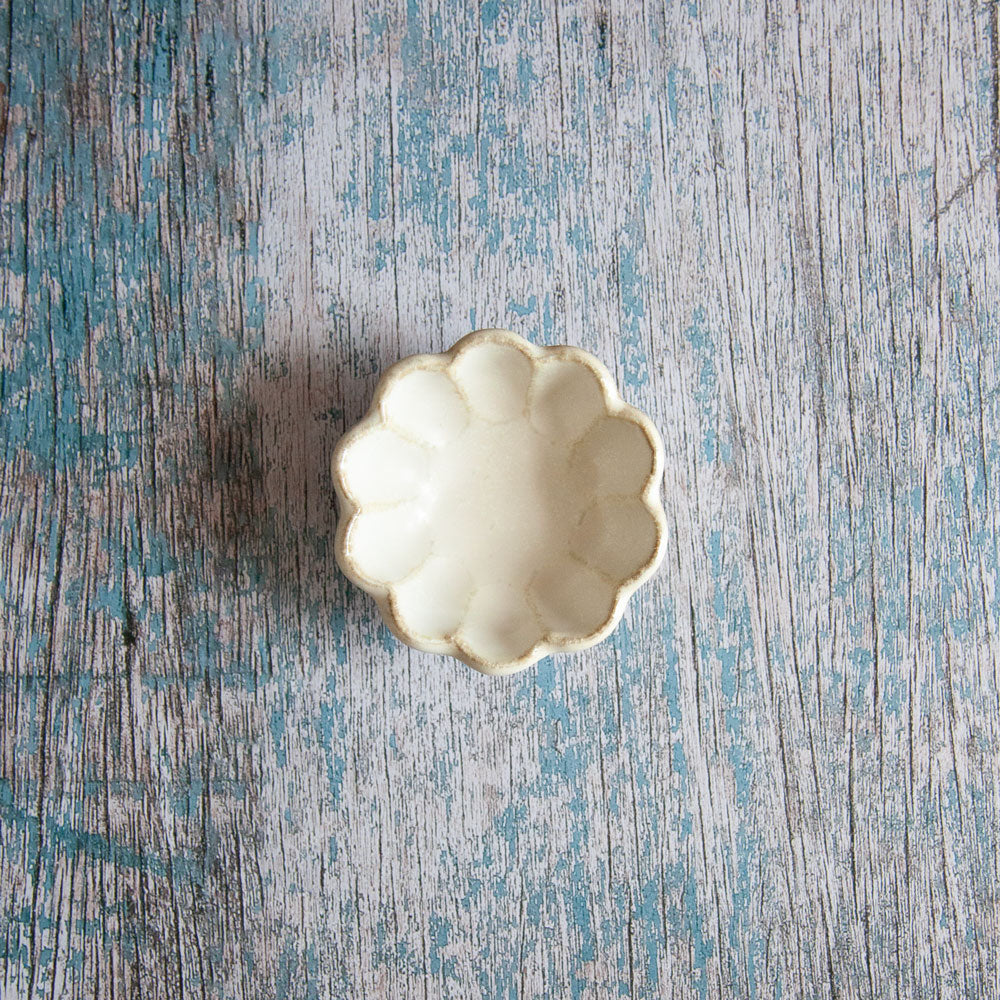 View from above of Rinka sauce dish. Small bowl with scalloped edged design resembling a flower. The dish is has three small feet. 