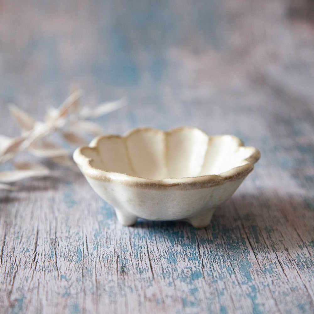Rinka sauce dish. Small bowl with scalloped edged design resembling a flower. The dish is has three small feet. 
