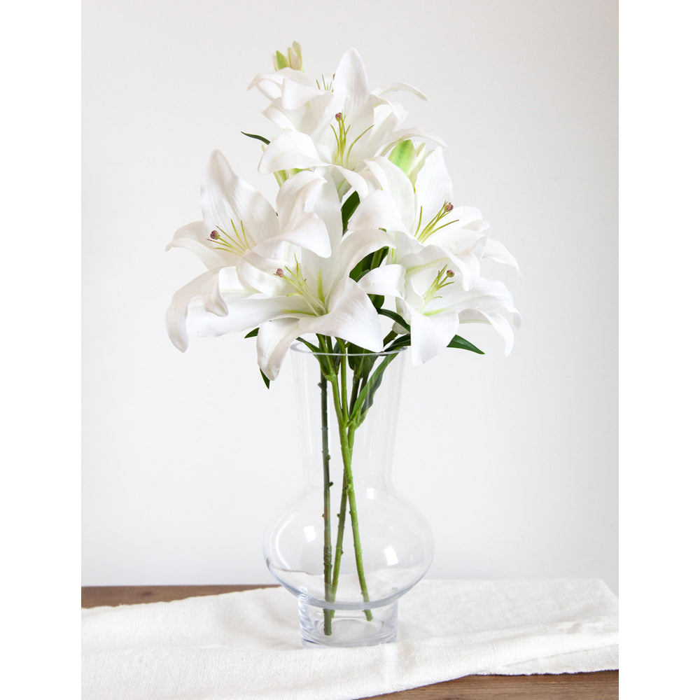 White artificial lilies in tall glass vase.