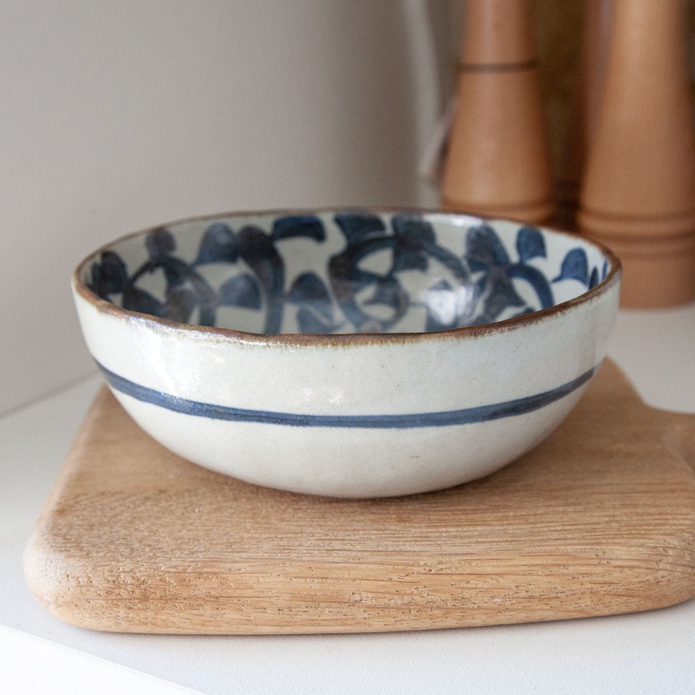Oval ceramic bowl with hand painted vine design on the inside surface and blue stripe around the outside.