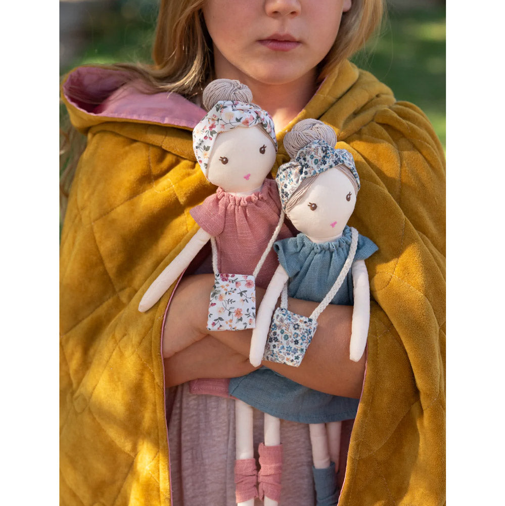 Young girl holding two rag dolls. One in a blue dress and one in pink. 