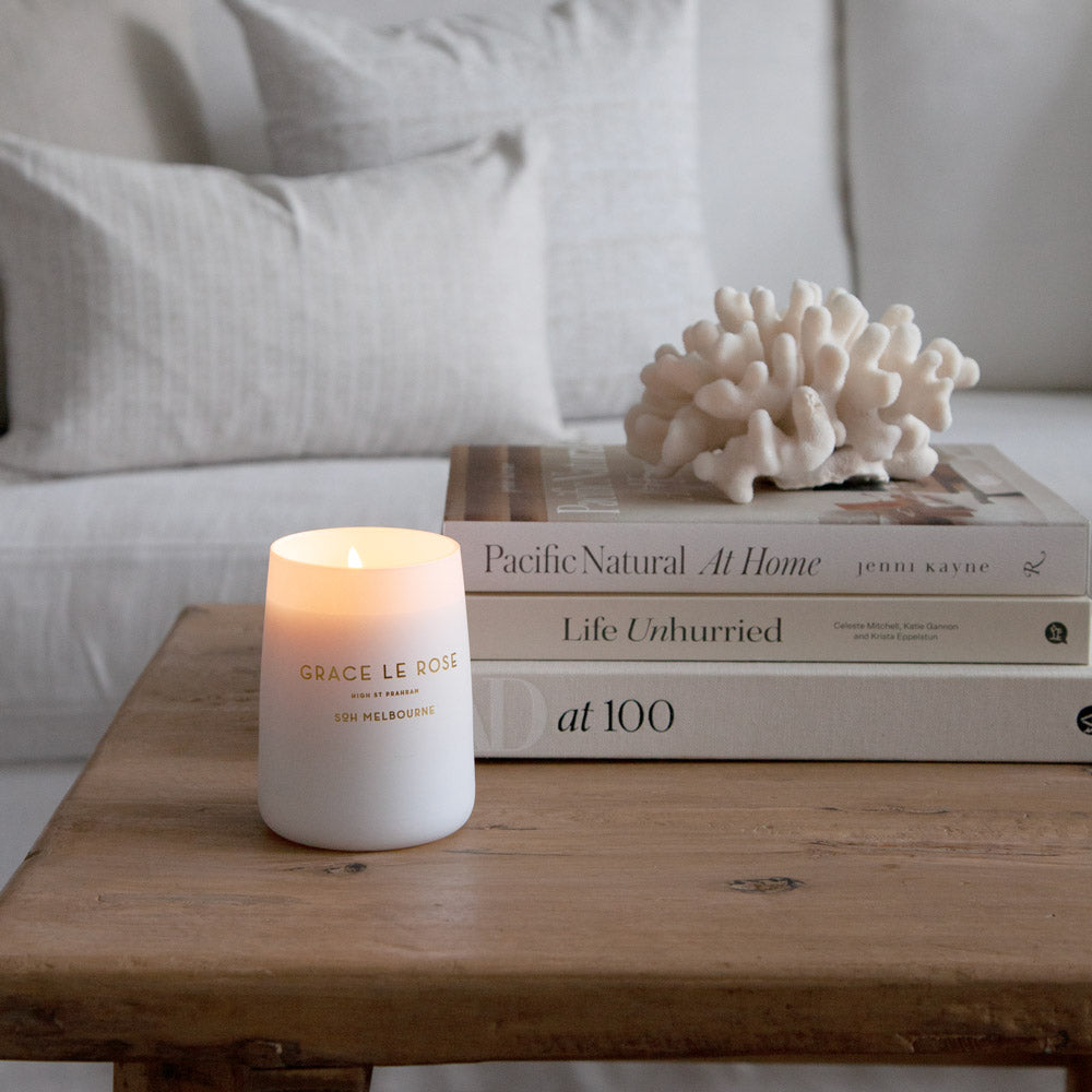 Grace Le Rose candle lit styled on a coffee table with books and coral.