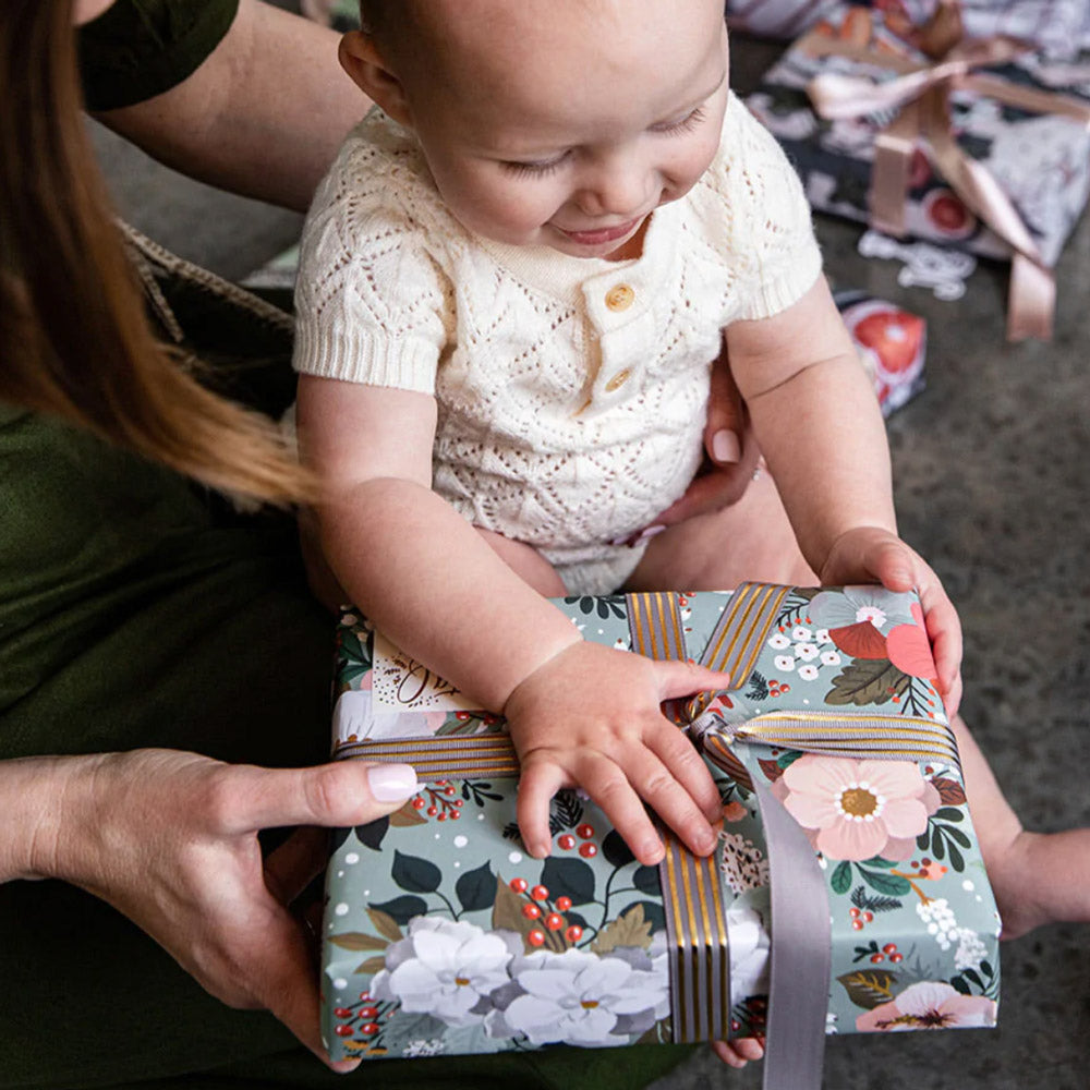 Baby holding Christmas gift wrapped using grey and gold ribbon.