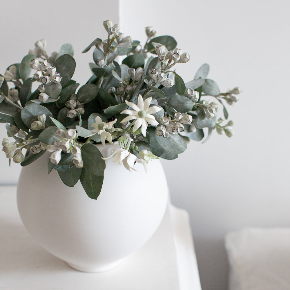 Artificial flannel flowers in large white vase with eucalyptus stems.