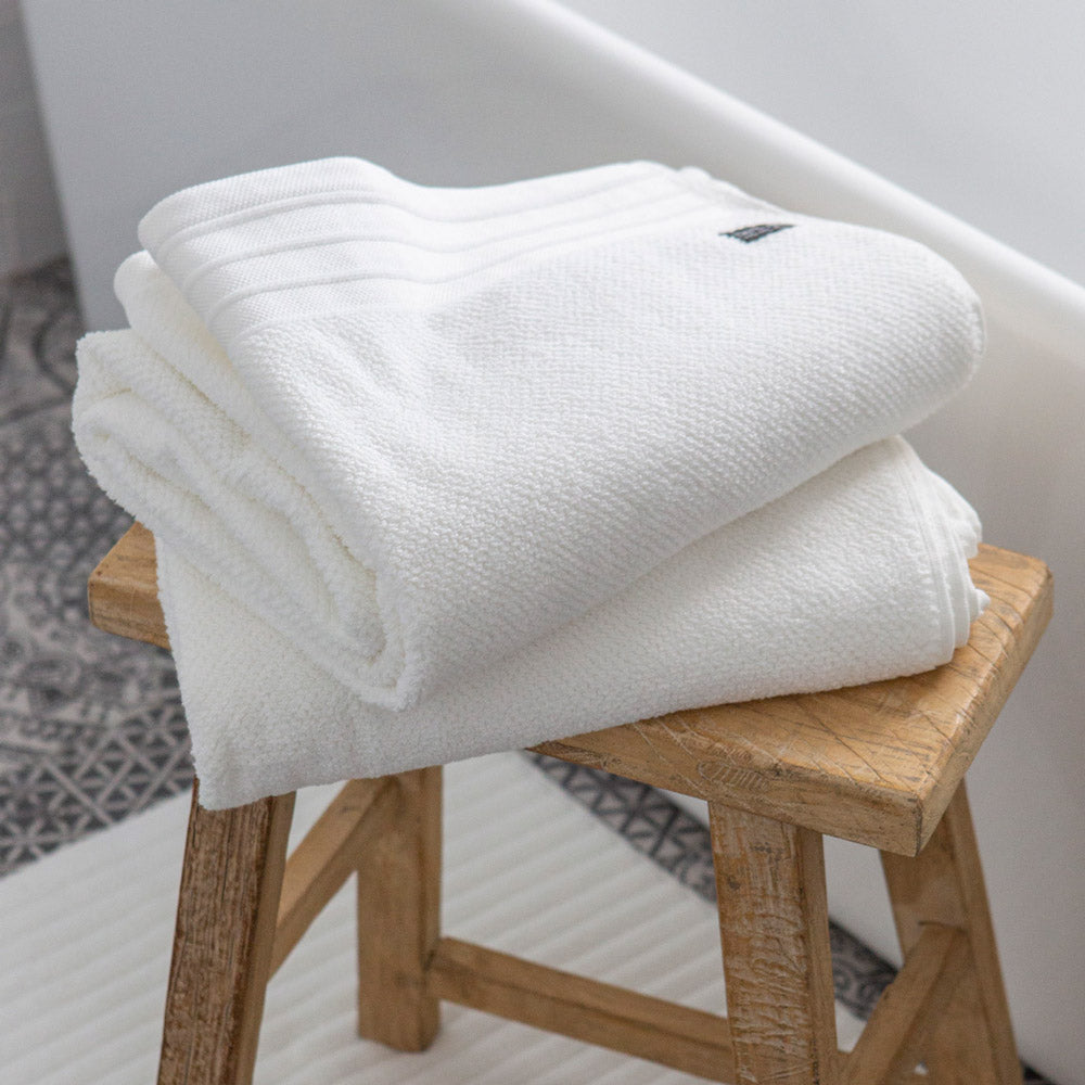 White Bemboka bath towels folded on wooden stool in bathroom