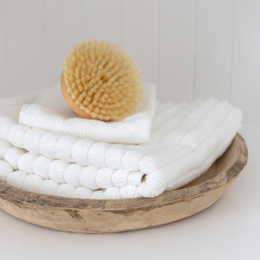 White Bemboka bath mat folded with hand towel and bath brush.